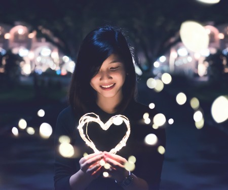 Woman holding a bright pink neon heart. Streams of light surrounding her.